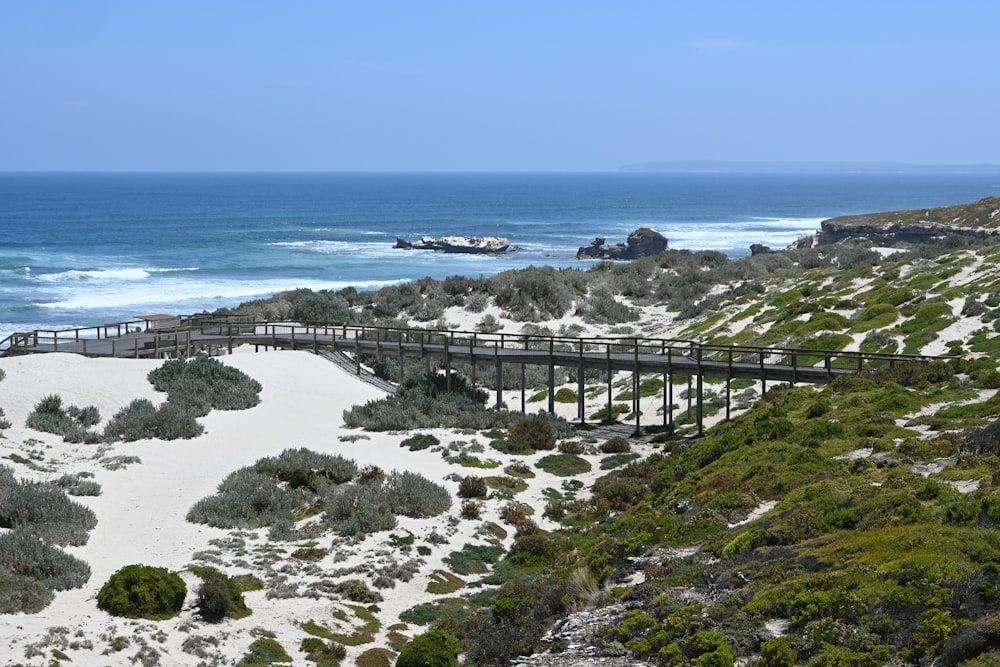 a wooden bridge over a sandy beach next to the ocean
