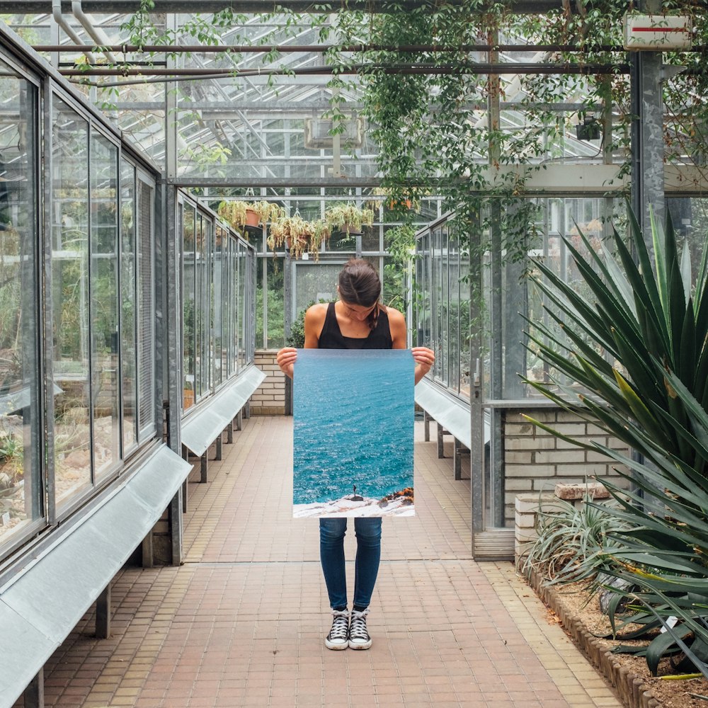 a woman holding up a picture in a greenhouse