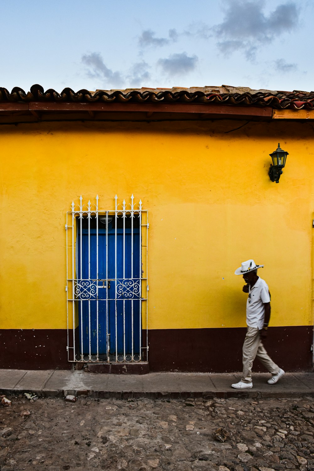 a man walking past a yellow building with a blue door