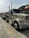 A large beige semi-truck is parked on a concrete road with a trailer attached. The vehicle has chrome details and the text 'BD 103' on the front. In the background, there is a hill with greenery and a flag with red, white, and green stripes. The sky is overcast.