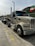 A large beige semi-truck is parked on a concrete road with a trailer attached. The vehicle has chrome details and the text 'BD 103' on the front. In the background, there is a hill with greenery and a flag with red, white, and green stripes. The sky is overcast.