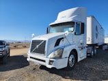 A semi-truck with a sleeper cabin parked against a Colorado mountain backdrop at sunrise.