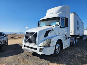 A pristine Freightliner semi-truck with a refrigerated trailer parked at a loading dock in bright daylight.