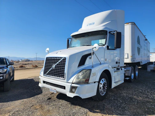 An owner-operator checking paperwork beside a parked semi-truck under a clear blue sky.