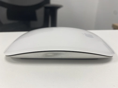 A Microsoft wireless mouse resting on a minimalist white desk, with a blurred Surface laptop in the background.