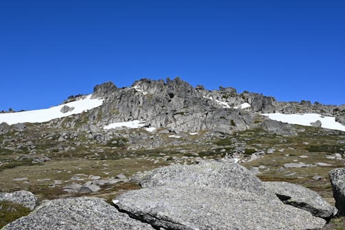 A rugged Patagonian mountain slope stabilized with stone-filled gabion walls under a clear blue sky.
