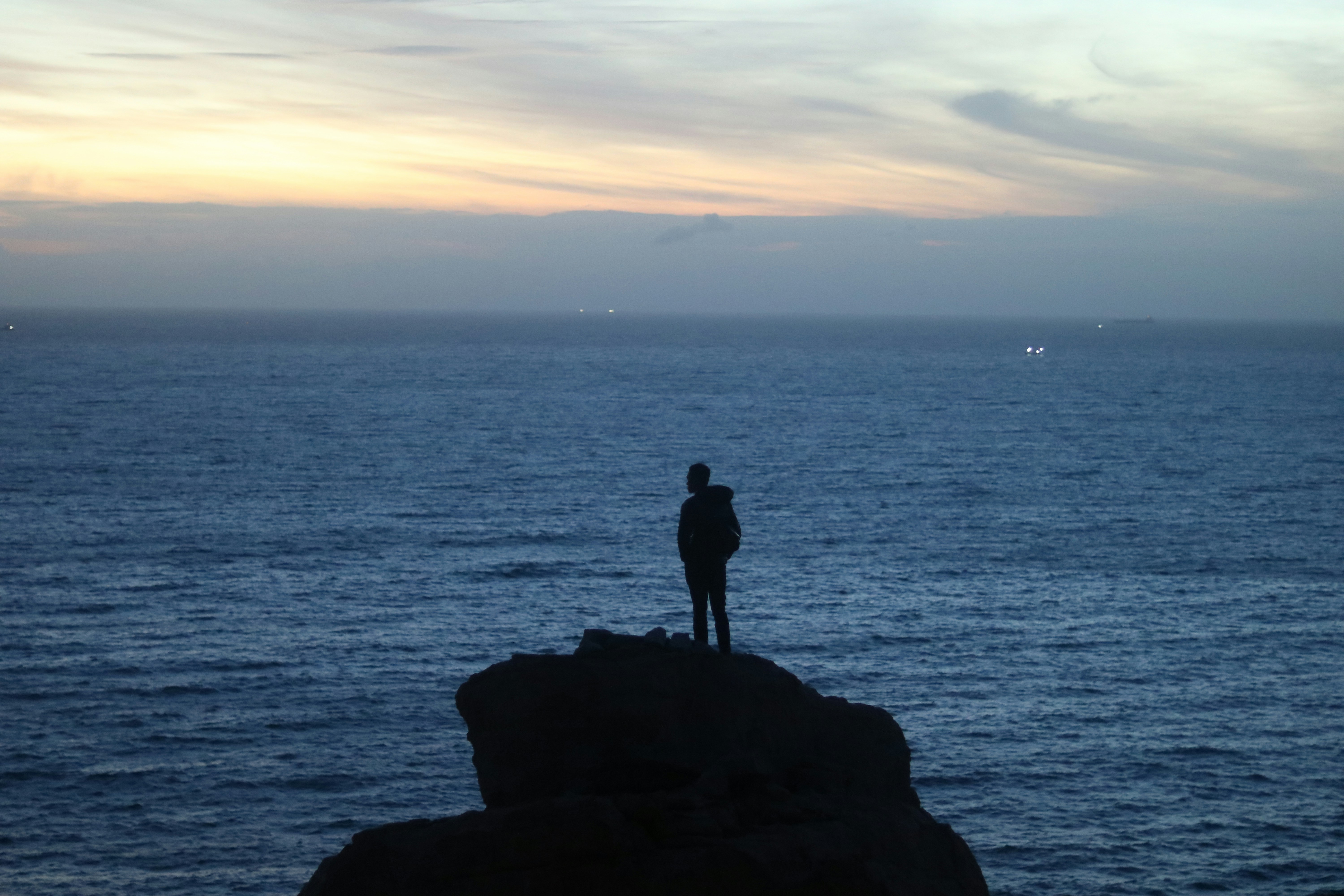 En siluett av en person som står vid kanten av en klippa och ser ut över ett vidsträckt hav.