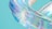 A digitally crafted, translucent swirl with iridescent colors reflecting a mix of blues, purples, and pinks on a pastel turquoise background. The material appears smooth and glossy, giving a sense of motion and fluidity.