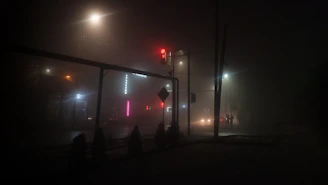 Foggy street at midnight with flickering neon motel signs in the distance.