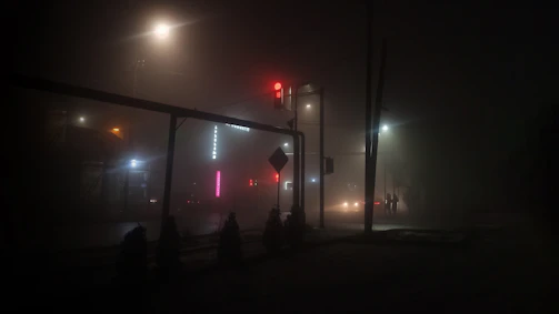 Foggy street at midnight with flickering neon motel signs in the distance.