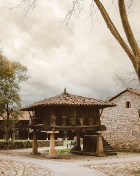 a stone building with a wooden roof next to a tree