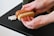 Hands are holding a wooden brush with natural bristles, positioned above a black surface. In the background, there are several cotton swabs partially visible.