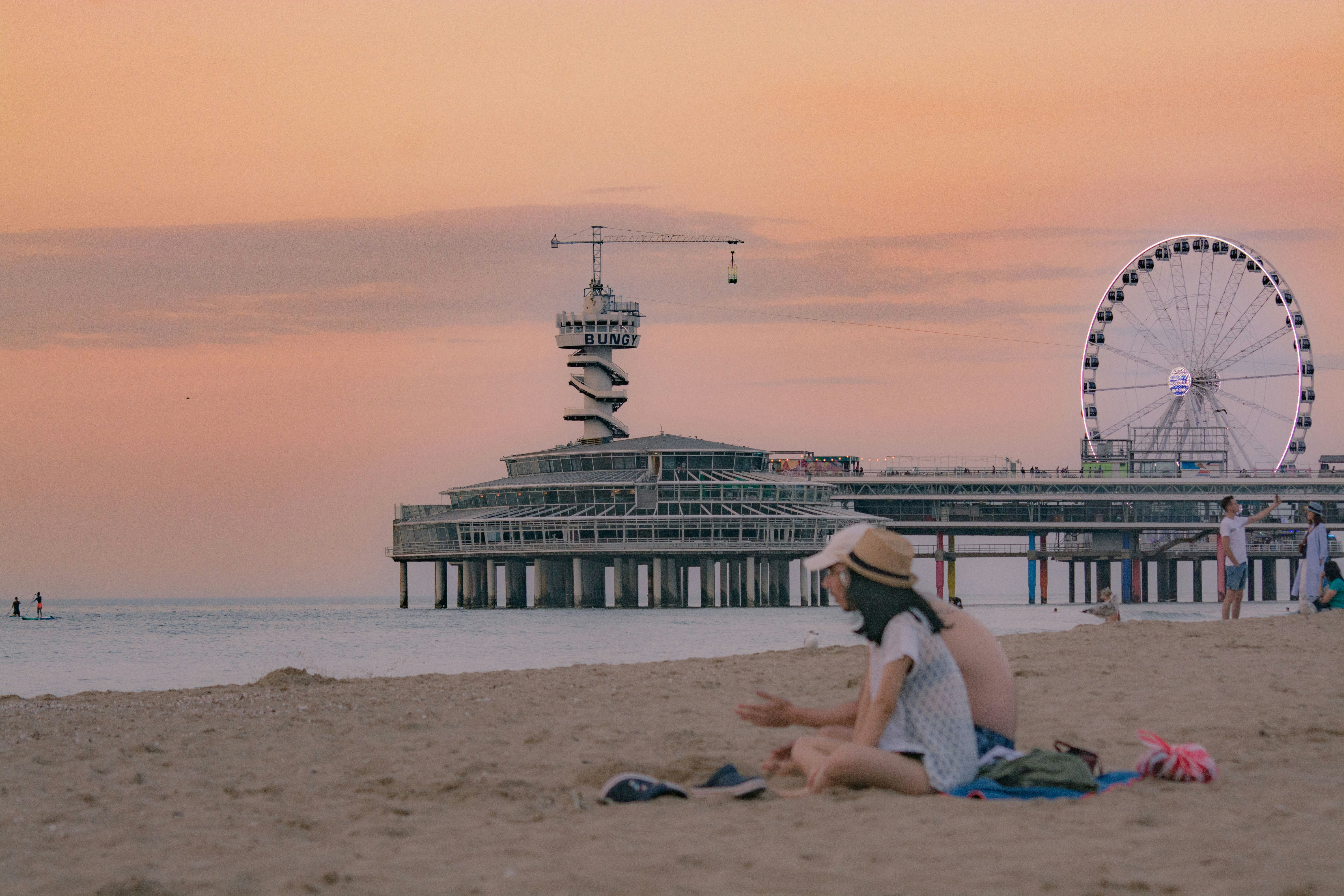 a woman sitting on top of a sandy beach next to a ferris wheel