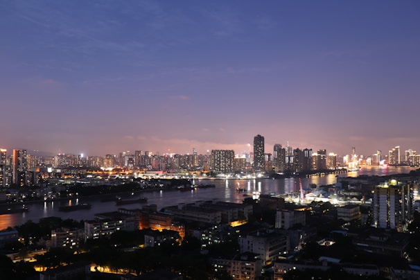 A bustling city skyline at dusk with glowing lights and a calm river reflecting the view