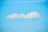 A fluffy white cloud floats in a clear blue sky. The cloud is centrally positioned with a soft, rounded shape, and the sky is bright and unobstructed.