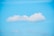 A fluffy white cloud floats in a clear blue sky. The cloud is centrally positioned with a soft, rounded shape, and the sky is bright and unobstructed.