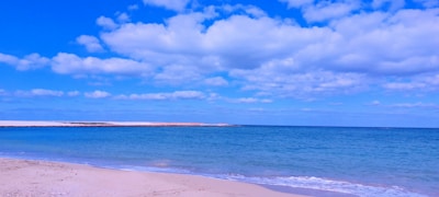 A calm beach with white sand and gentle waves under a clear blue sky.