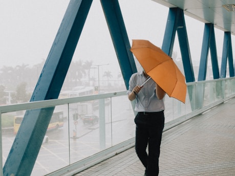 a man walking across a bridge while holding an umbrella