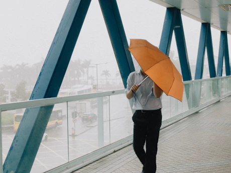 a man walking across a bridge while holding an umbrella