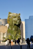 people walking around a building with a giant bear sculpture