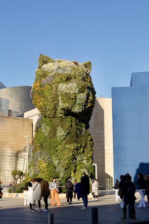 people walking around a building with a giant bear sculpture