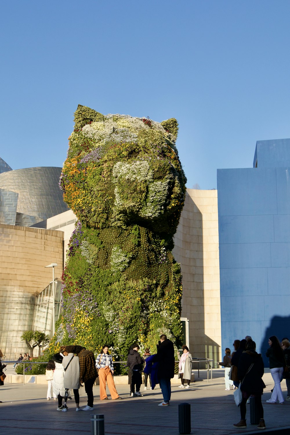 people walking around a building with a giant bear sculpture