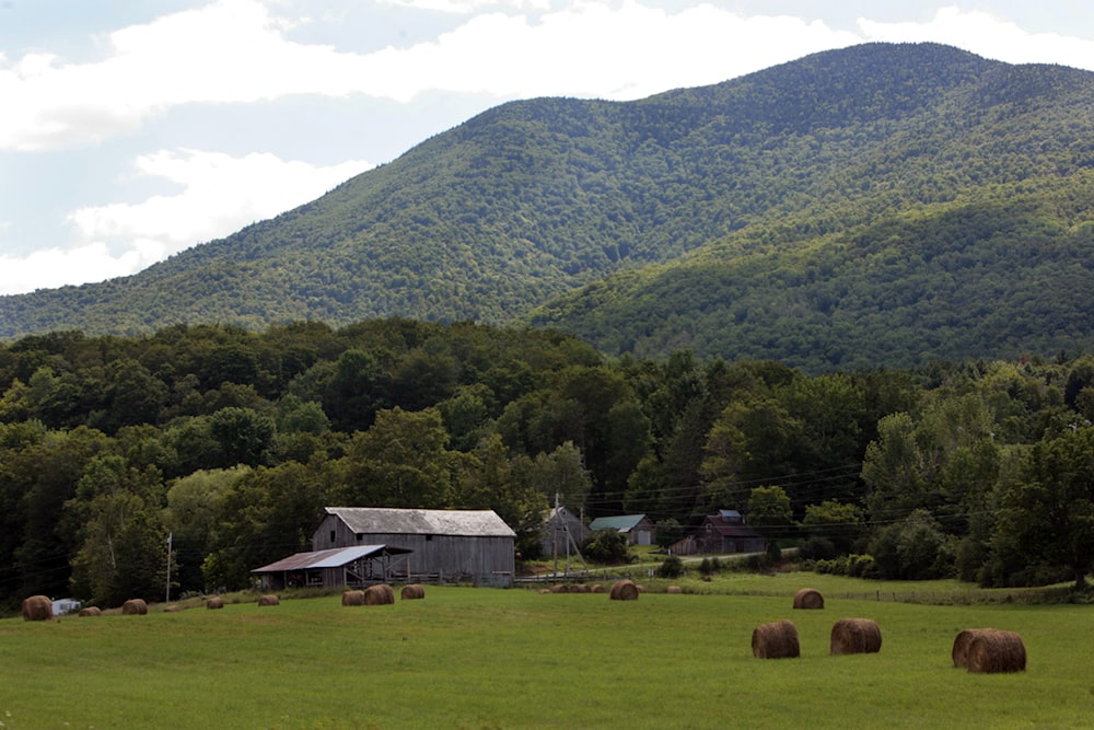 a large field with hay bales in the foreground and a barn in the