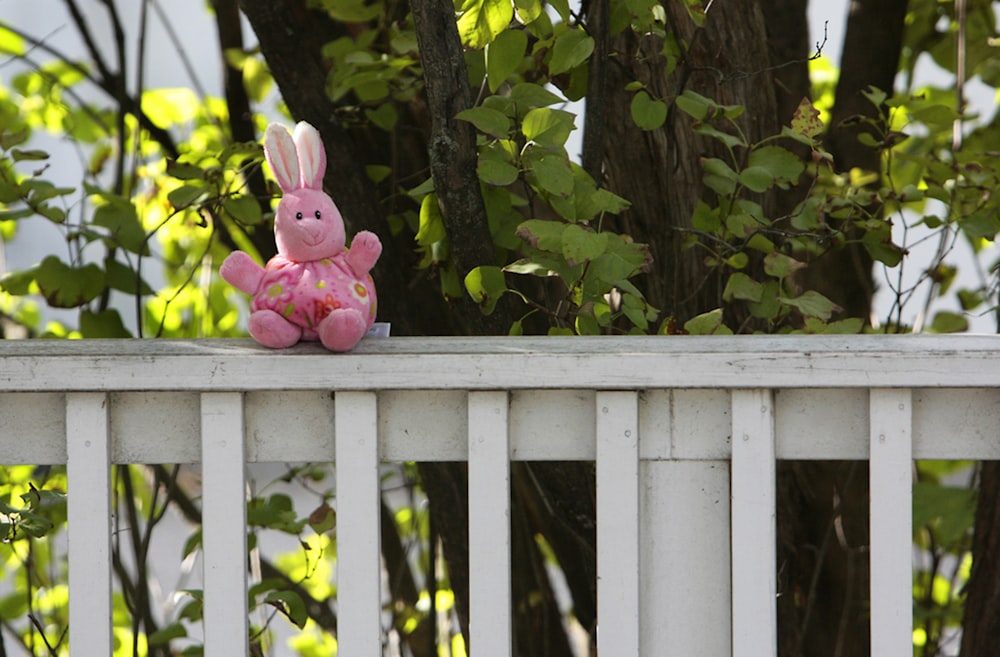a pink stuffed rabbit sitting on top of a white fence