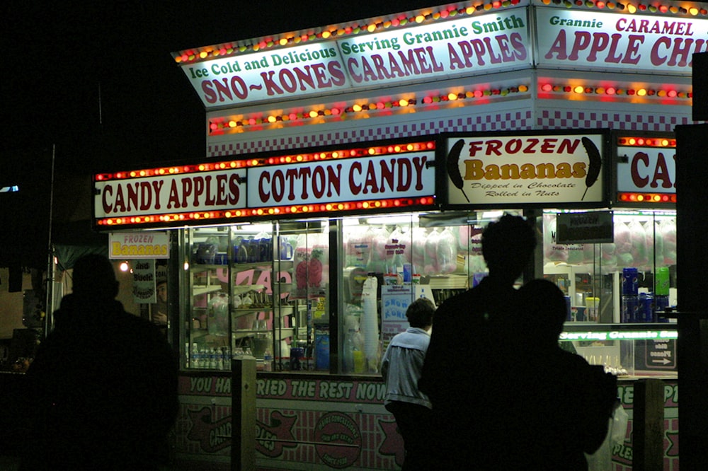 people are standing outside of a candy shop at night