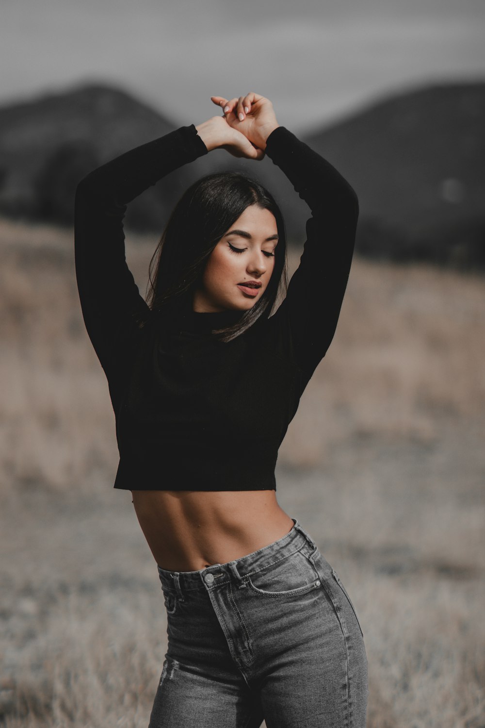 a woman standing in a field with her hands behind her head