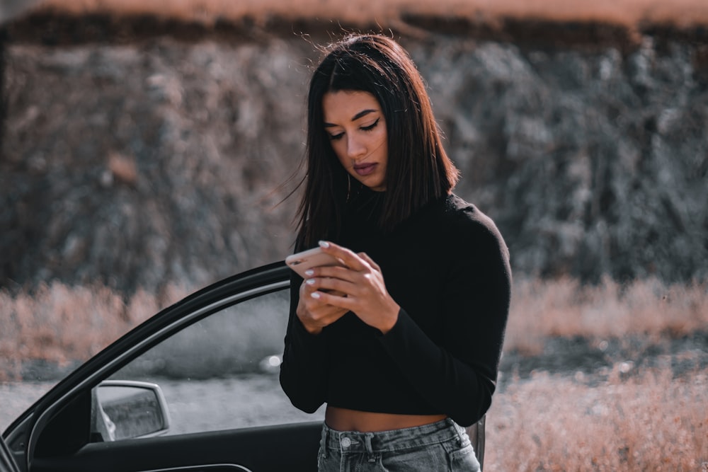 a woman standing next to a car looking at her cell phone