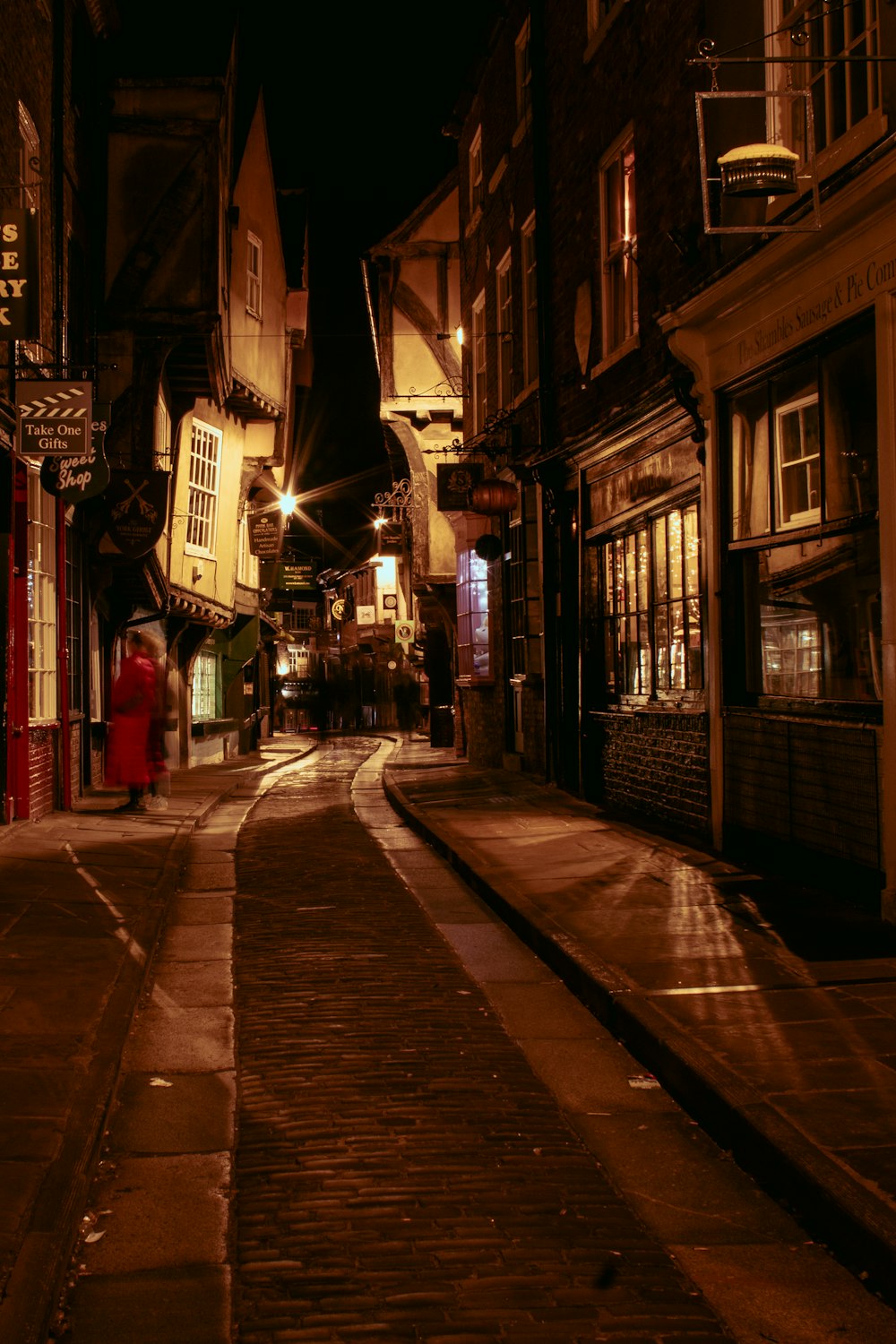 a narrow street at night with a red fire hydrant