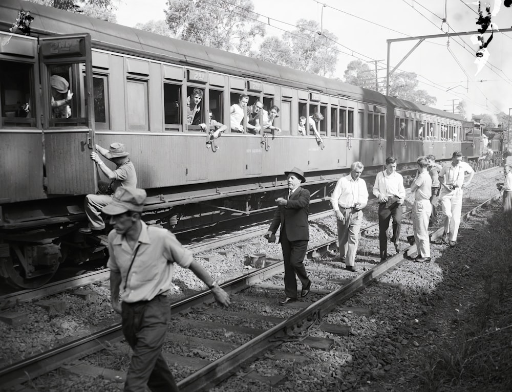 uma foto em preto e branco de um grupo de pessoas andando em um trilho de trem