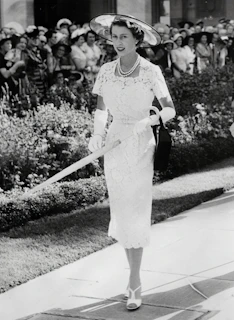 A fashionable woman in a flowing white formal dress with delicate lace details, walking through a sunlit European garden.