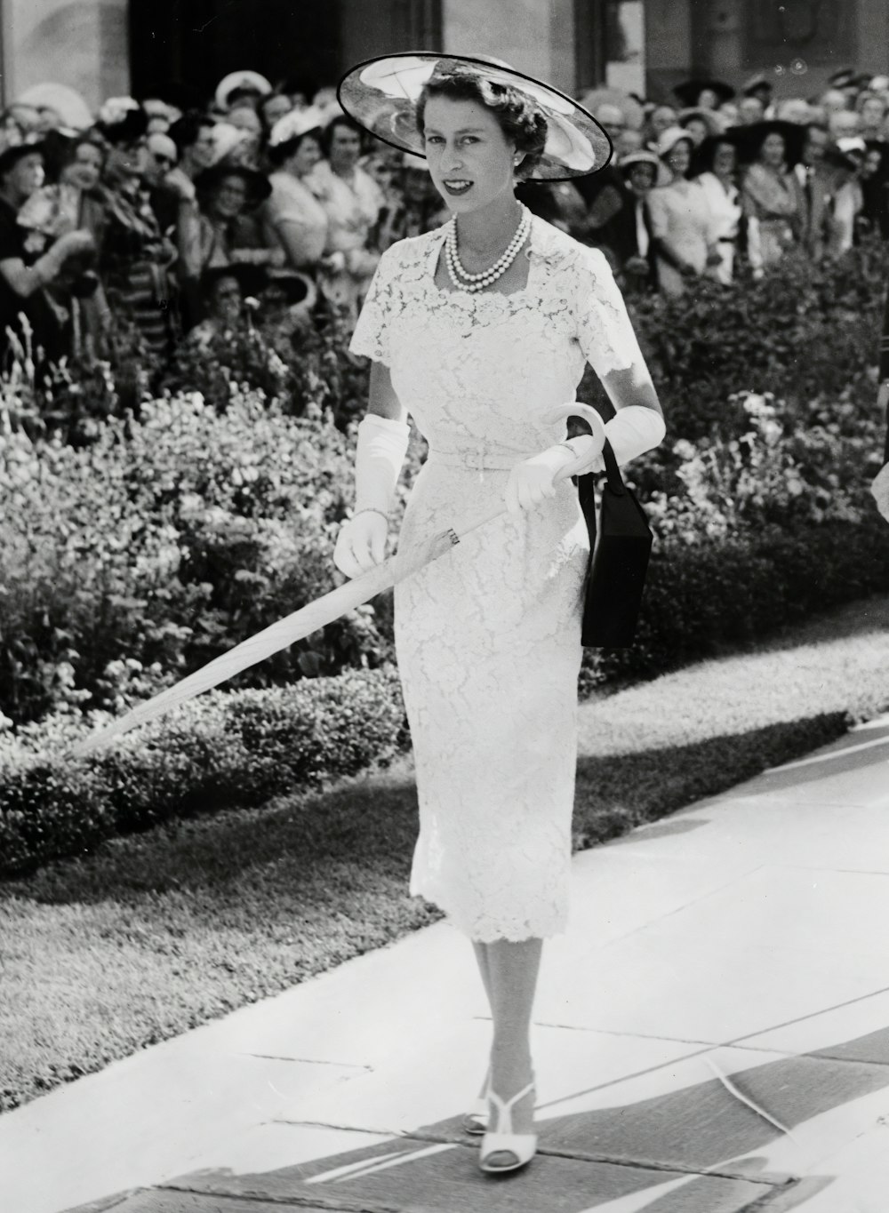 흰 드레스와 모자를 쓴 여자가 보도를 걷고 있다