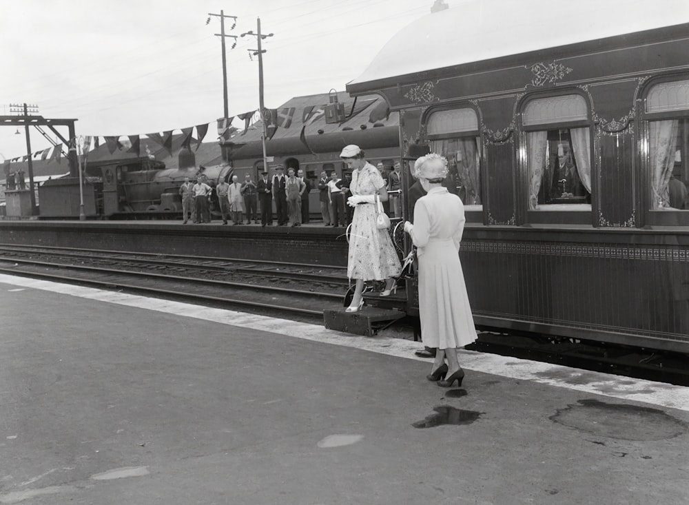 a black and white photo of a woman standing next to a train
