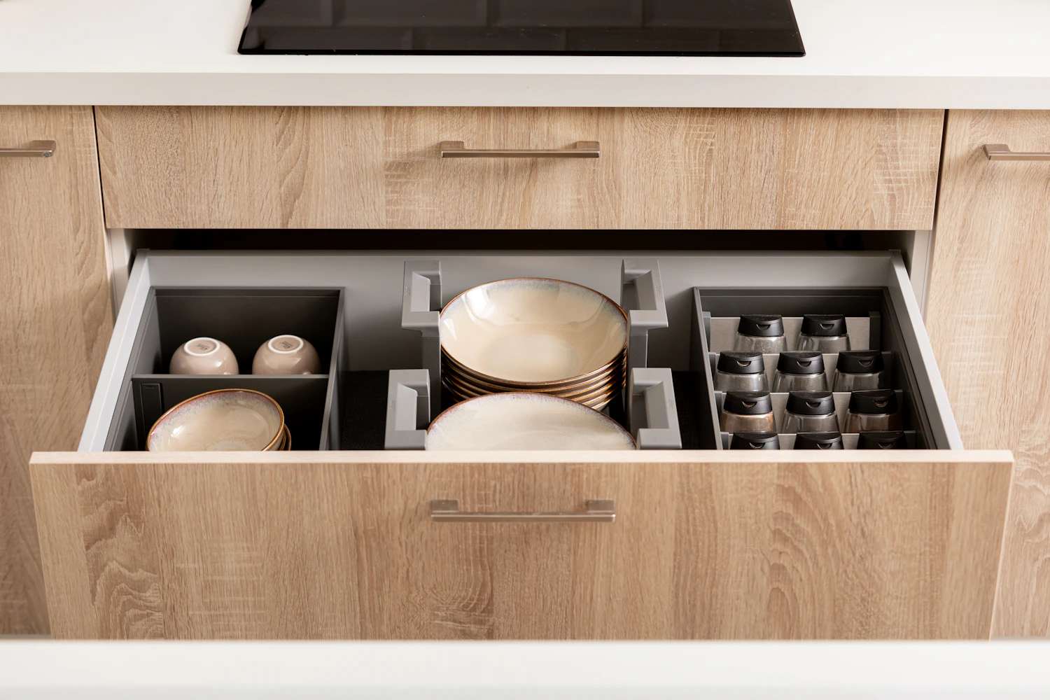 Organized kitchen drawer holding plates spices and cups in fitted storage sections