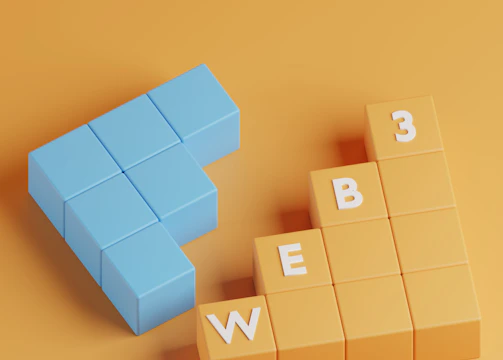 A three-dimensional arrangement of blocks on a solid orange background. The blue blocks are shaped like an arrow pointing left, and the orange blocks are stacked like steps with white letters spelling 'WEB 3'.