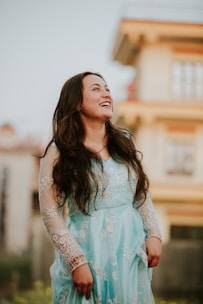 A fashionable woman in a chic dress, smiling softly with a cityscape behind her.