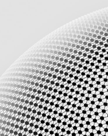 A close-up view of a geometric pattern consisting of black spherical nodes connected by thin lines, forming a lattice structure on a curved surface. The background is a light gray gradient.