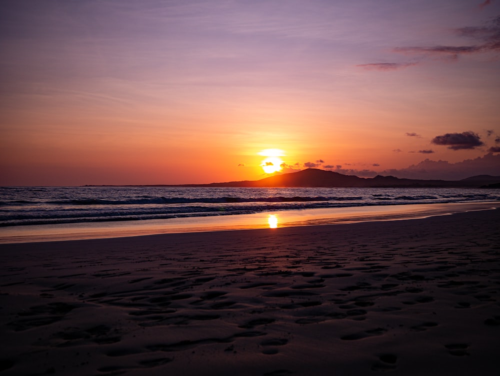 the sun is setting over the ocean with footprints in the sand