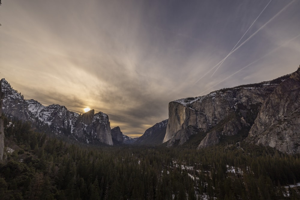 the sun is setting over the mountains and trees