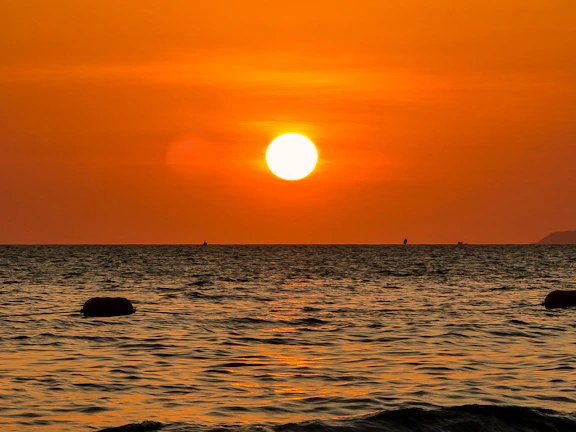 A vibrant painting of a sunset over a calm sea, with warm orange and pink hues.