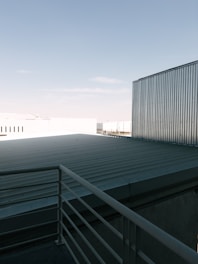A rooftop with a metal railing and corrugated metal sheets under a clear blue sky. The scene includes industrial-looking buildings with metallic textures.