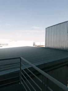 A skilled roofer installing metal sheets on a modern industrial building under clear skies.
