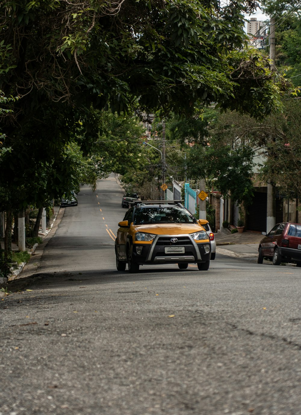 a yellow car driving down a street next to trees