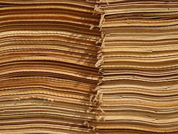 Stacks of thin, unevenly cut wooden sheets create a visually intricate and textured pattern. The sheets vary in color, ranging from light tan to deep brown, and appear to be layered in an organized manner.