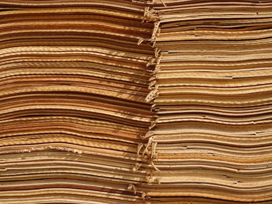 Stacks of thin, unevenly cut wooden sheets create a visually intricate and textured pattern. The sheets vary in color, ranging from light tan to deep brown, and appear to be layered in an organized manner.