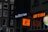 Storefronts in an urban setting feature brightly lit signs. 'Royal Queen Seeds' is illuminated in white, while 'Wok to Walk' is in bold orange lettering. A side image shows a stylized figure holding a wok.