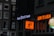 Storefronts in an urban setting feature brightly lit signs. 'Royal Queen Seeds' is illuminated in white, while 'Wok to Walk' is in bold orange lettering. A side image shows a stylized figure holding a wok.